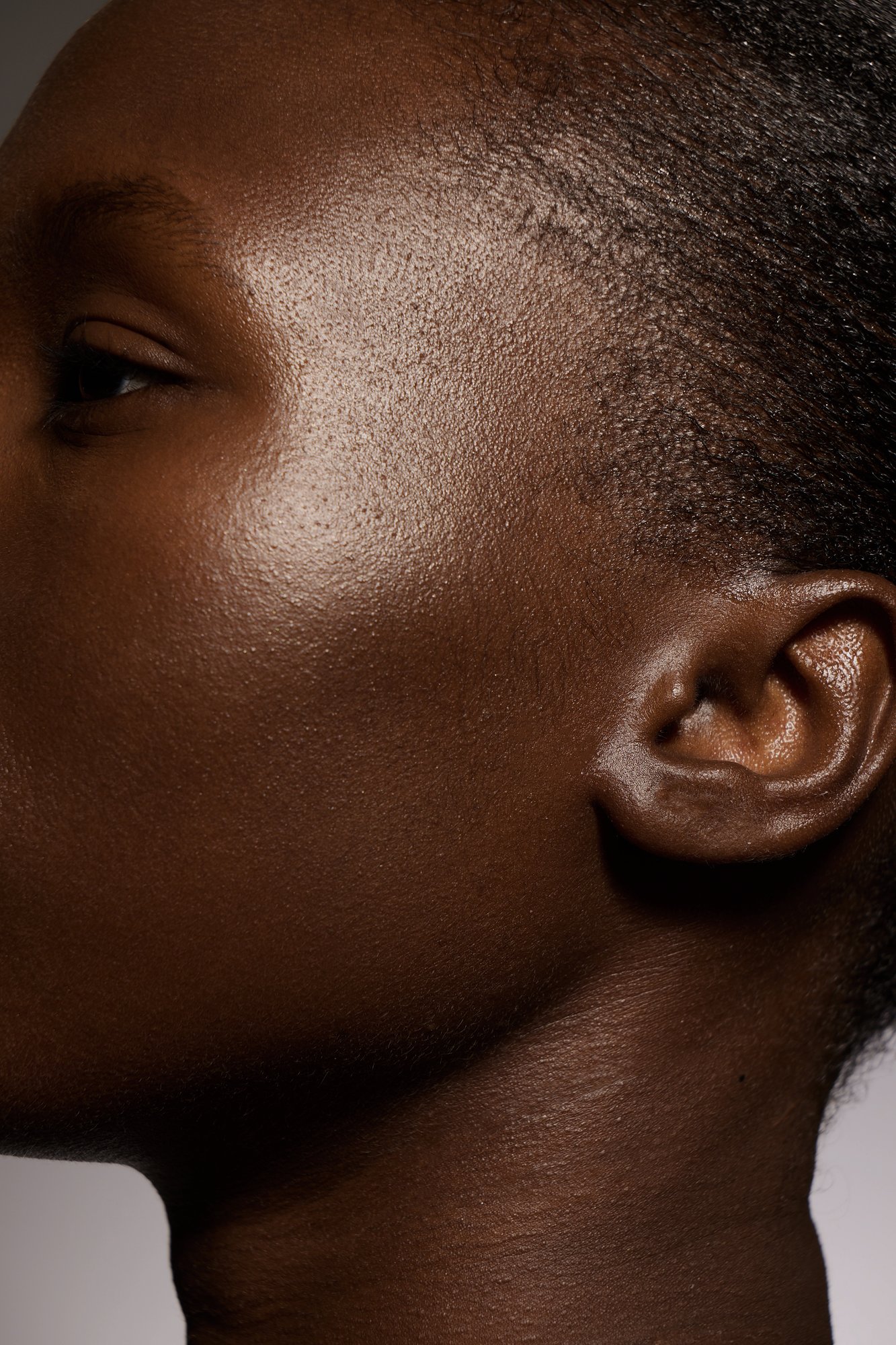 Extreme close-up in profile of a woman's cheek, ear and hairline under soft studio light