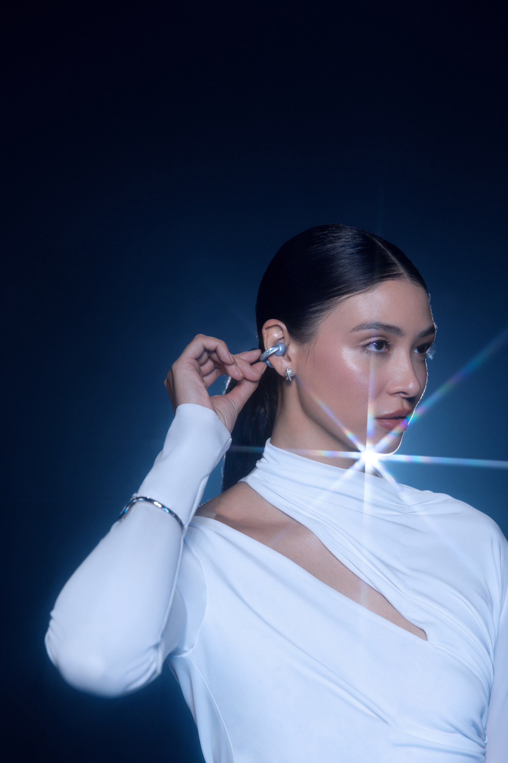 Woman in a white top touches her crystal ear cuff as a starburst of light flares beside her face