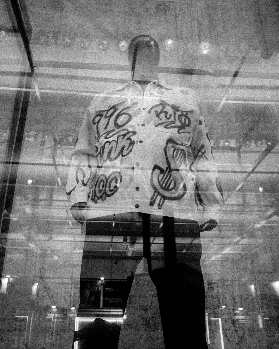 Black and white view through glass of a mannequin wearing a graffiti-painted jacket
